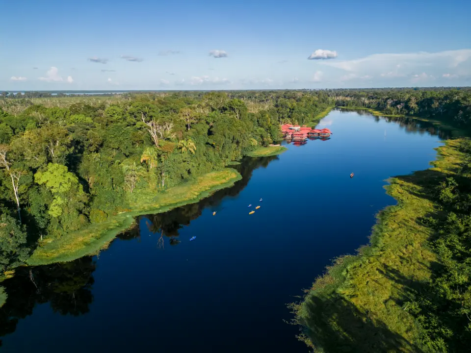Vista aérea de un río que serpentea entre la selva amazónica con un alojamiento de techos rojos al fondo