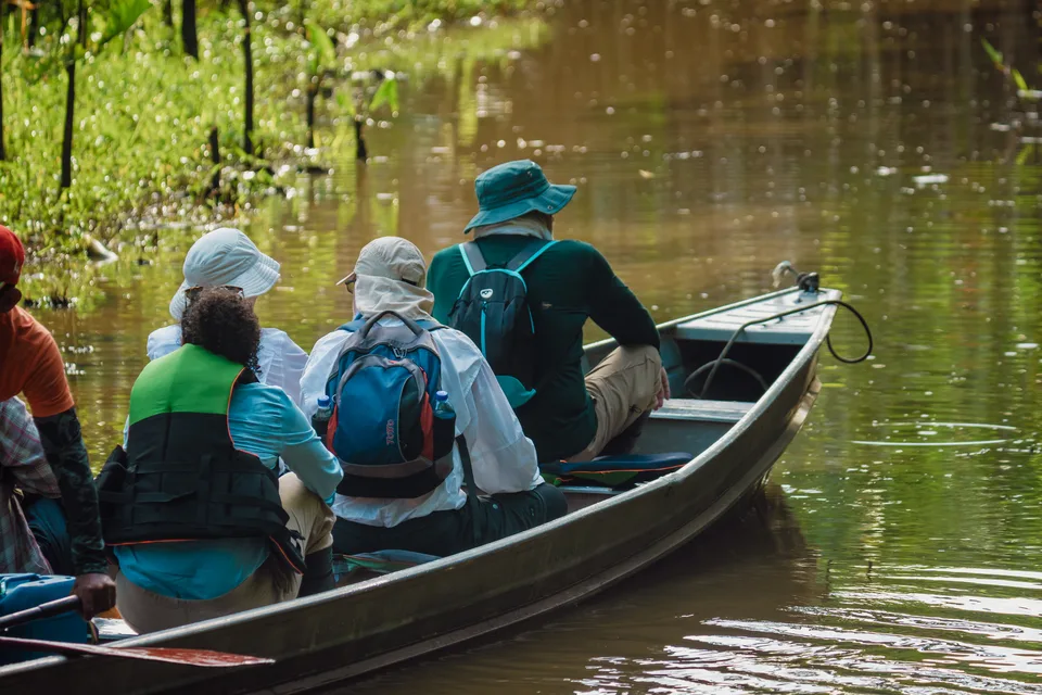 Turistas en una lancha de madera por un río de selva, vistos desde atrás